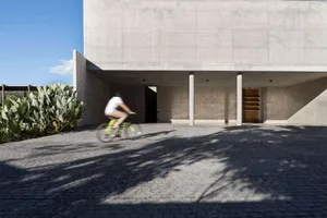 A cyclist riding on a cobblestone path near a minimalist concrete building.