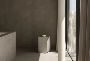 Modern minimalist bathroom featuring a concrete floor and walls, with a white pedestal and greenery.