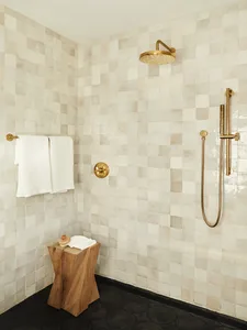 Minimalist bathroom with white tiles, a wooden stool, and brass fixtures.