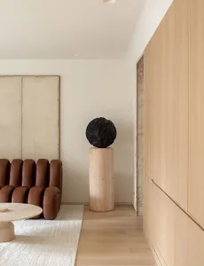 A minimalist living room featuring a wooden floor, light-colored wooden furniture, and abstract art.