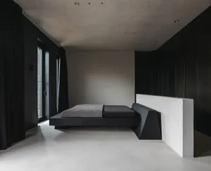 A minimalist bedroom with black and white decor, featuring a concrete bed platform with a geometric headboard.
