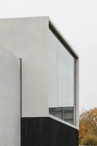 Modern architectural exterior featuring concrete and black wooden panels with a large glass window.