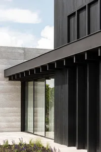Modern building exterior with concrete and wooden panels, featuring glass windows and a minimalist design.
