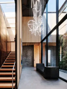 A modern, industrial-style interior with concrete walls, wooden stairs, and a large glass wall.