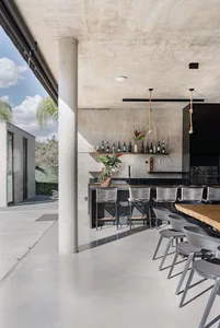 An indoor modern kitchen with concrete and glass materials, featuring a bar area with bottles and stools.