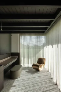Modern living room featuring a metal chair, fabric window treatments, and a large window overlooking a serene outdoor view.