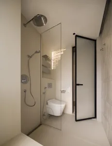 Modern, minimalist bathroom featuring a tiled shower enclosure with glass walls and metal fixtures.