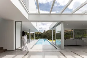 A modern residential interior with a sleek, minimalist design featuring a concrete floor, large windows, and a view of a swim