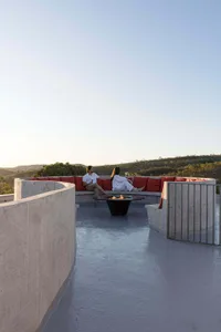 A couple sitting on a concrete rooftop with red cushions and a fire pit, overlooking a scenic landscape
