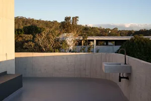 A minimalist concrete patio with a sleek sink and a view of surrounding trees and buildings.