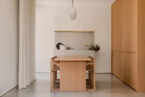 A minimalist residential kitchen with concrete walls, wood accents, and a dining table