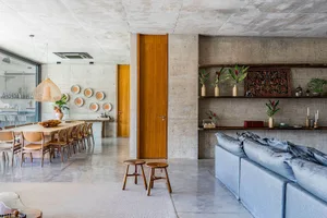A modern interior design featuring a living and dining room with concrete walls, wooden doors, and a grey sofa.
