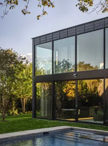 Modern house with large glass windows and a concrete base featuring a pool.