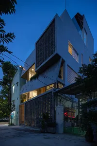 A modern residential house exterior at night, featuring concrete textures and illuminated interiors.