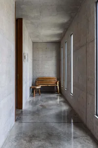 A minimalist, modern interior space featuring a concrete floor and walls, with a wooden bench in the center.