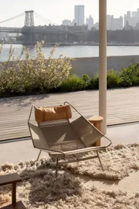 Modern rooftop lounge area featuring a leather-textile lounge chair with a wooden deck, plants, and a view of the city and br