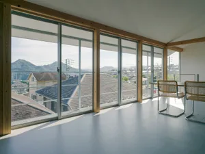 Modern apartment with large windows overlooking mountains, featuring wood, glass, and concrete materials.