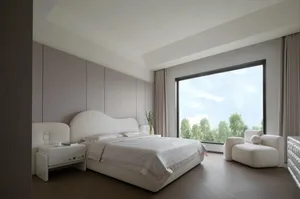 A minimalist bedroom with a large window, fabric blinds, a bed with white bedding, and a white armchair.
