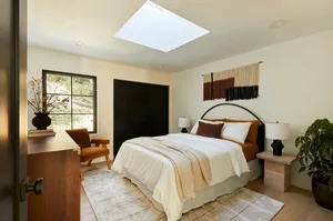 A minimalist bedroom with a white bed, brown cushions, and a skylight above a wooden floor.