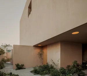 A minimalist house with a concrete exterior, featuring a small garden with green plants.
