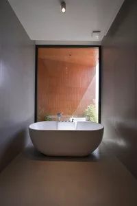 Modern minimalist bathroom with a white freestanding bathtub, ceramic tiles, and a large window showing greenery.