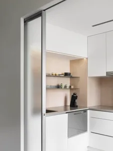 A modern, minimalist kitchen with white cabinets, open shelves, and sleek, clean lines.