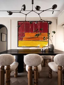 A modern dining room with a wooden table and chairs, featuring a colorful abstract painting and a chandelier with multiple li