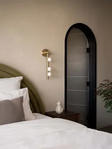 A modern bedroom with a fabric headboard, glass sconce, and white bed.