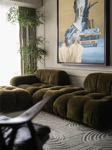 A modern living room featuring a plush, olive-green velvet sofa with a contemporary abstract painting above it, accompanied b