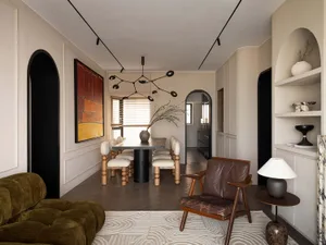 A minimalist dining room with wooden furniture, featuring a black circuit-like pendant light, beige walls, and a patterned ru