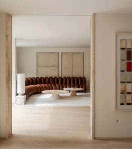 A modern minimalist living room with a brown leather sofa, two marble tables, and abstract art on the wall.