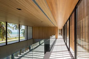 Modern industrial corridor with timber ceiling and walls, featuring large windows and a glass railing.