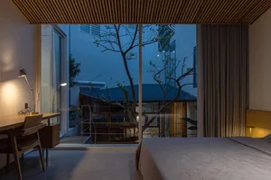 A minimalist bedroom with a wooden bed, desk, and ceiling design, featuring a large window overlooking a courtyard with trees