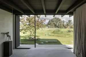 A minimalist bedroom with wood elements and a view of greenery through a large window.