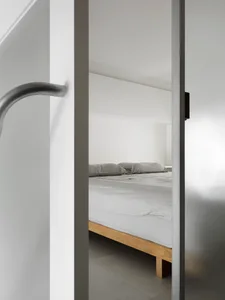 A minimalist bedroom featuring a wooden bed frame and grey bedding on a white bed sheet.