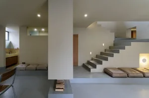 極簡客廳，混凝土牆面與樓梯，搭配柔軟座椅與現代設計。
