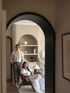 Two people sitting in a minimalist living room with wooden furniture, marble accents, and fabric elements.