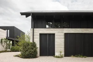 Black and concrete modern architectural exterior with black windows and doors, surrounded by gravel and green shrubs.