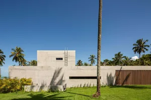 A modern building with a concrete exterior surrounded by green grass and palm trees.
