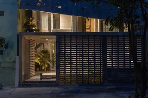 Modern house exterior featuring concrete walls with a grid pattern and illuminated windows at night.