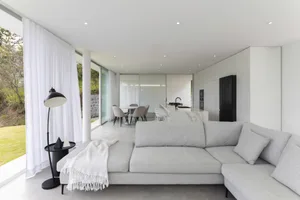 Contemporary living room featuring a large concrete sofa and floor-to-ceiling windows.