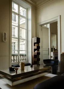A modern living room featuring a metallic table with decorative objects on it, viewed through a tall, multi-paned window.