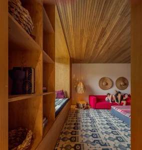 A cozy modern living room with wooden furniture and a vibrant pink sofa, featuring built-in shelves, a patterned rug, and wov