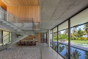 A spacious, modern dining area with concrete flooring, large glass windows, wooden accents, and a concrete staircase.