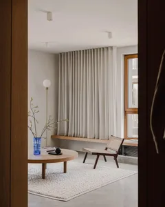 A minimalist living room featuring wood elements, a round coffee table, a tall floor lamp, and a contemporary chair.