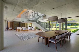 Modern interior design featuring open-plan living spaces with concrete and glass elements overlooking a garden.