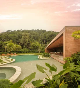 Modern outdoor lounge area featuring a natural stone pool edge surrounded by lush greenery at sunset.