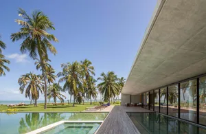 A modern poolside villa featuring concrete and glass materials, with a pool, palm trees, and a spacious outdoor area.