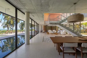 Modern residential interior with concrete and glass materials, featuring a large dining area and living space.