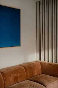 Modern sitting room featuring a brown velvet sofa and a blue artwork on the wall.